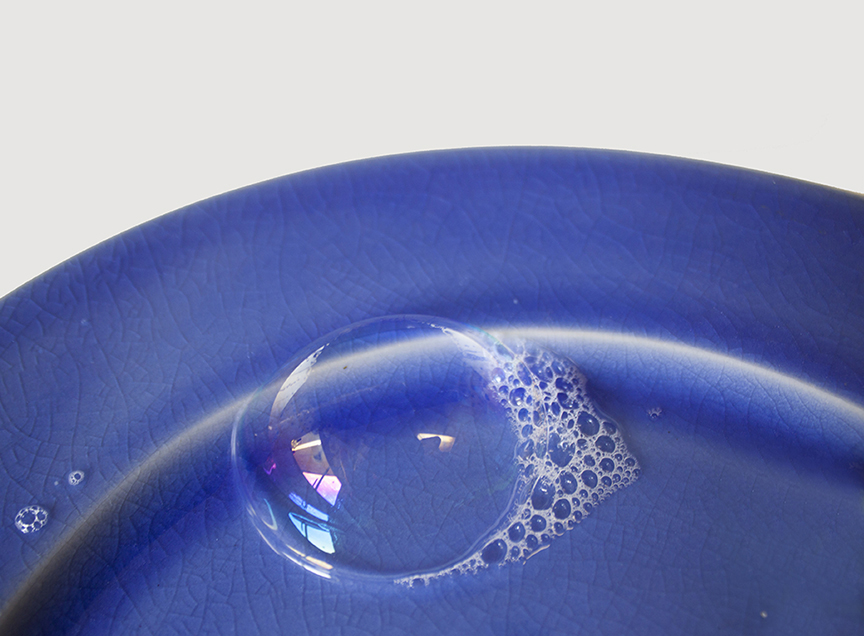 large bubble and soap suds on bright cobalt blue plate against w