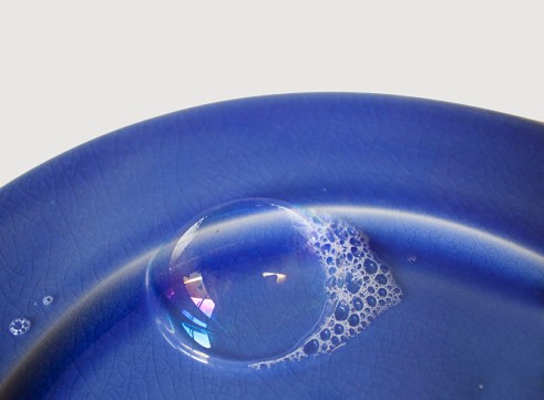 large bubble and soap suds on bright cobalt blue plate against w